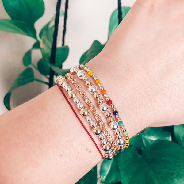 Model wearing stack of mixed metal bracelets, gold rope bracelet, and rainbow czech glass beaded bracelet