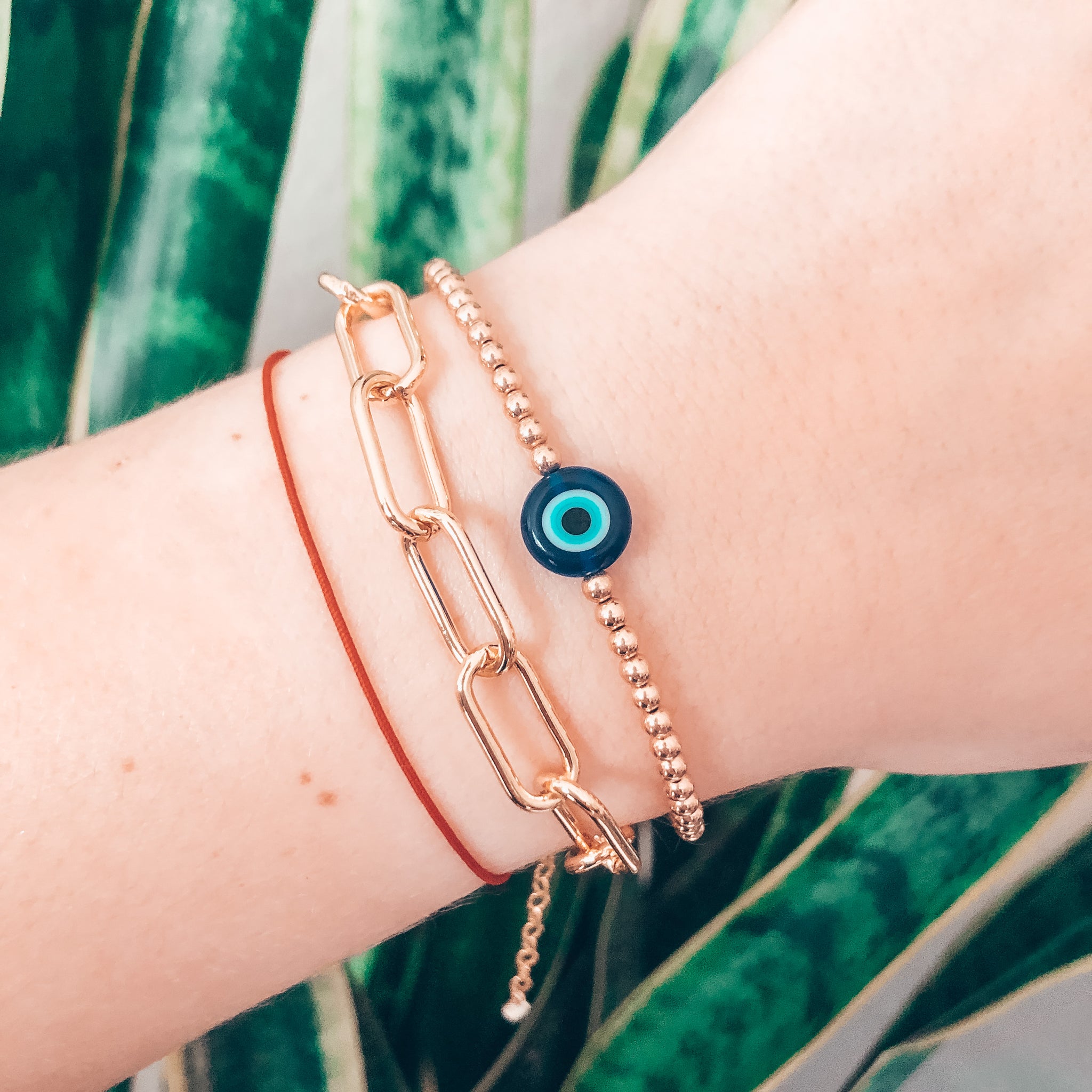 Model photo wearing Gold thick link chain bracelet with extender and evil eye beaded bracelet