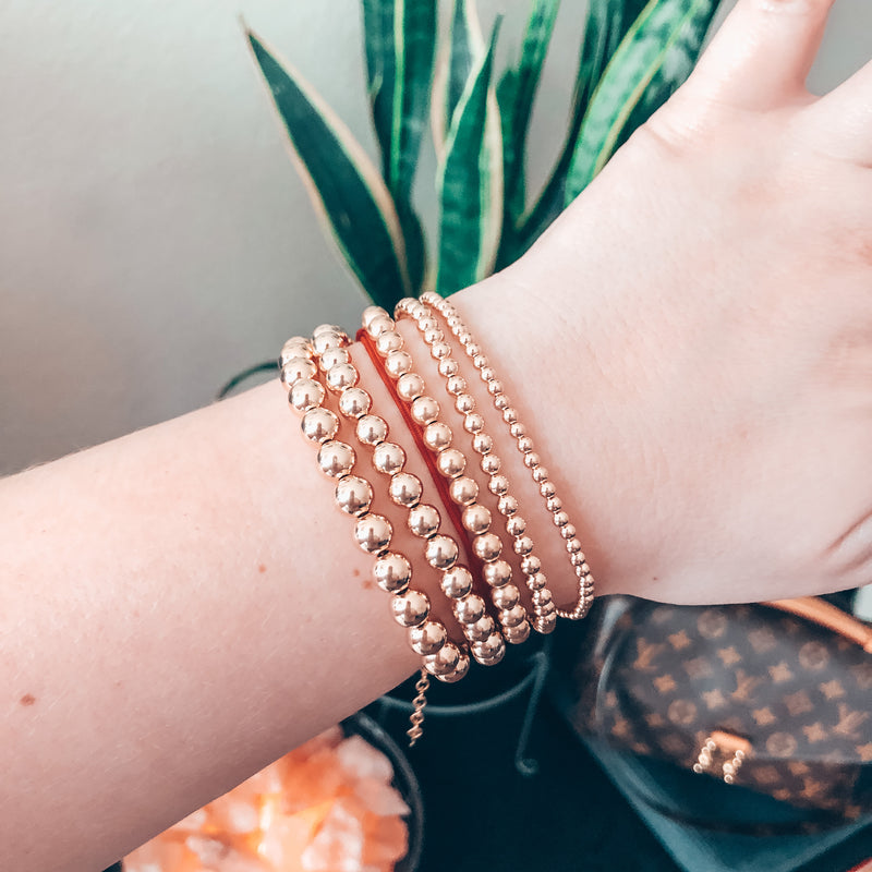 Model photo of wrist wearing stack of beaded gold bracelets