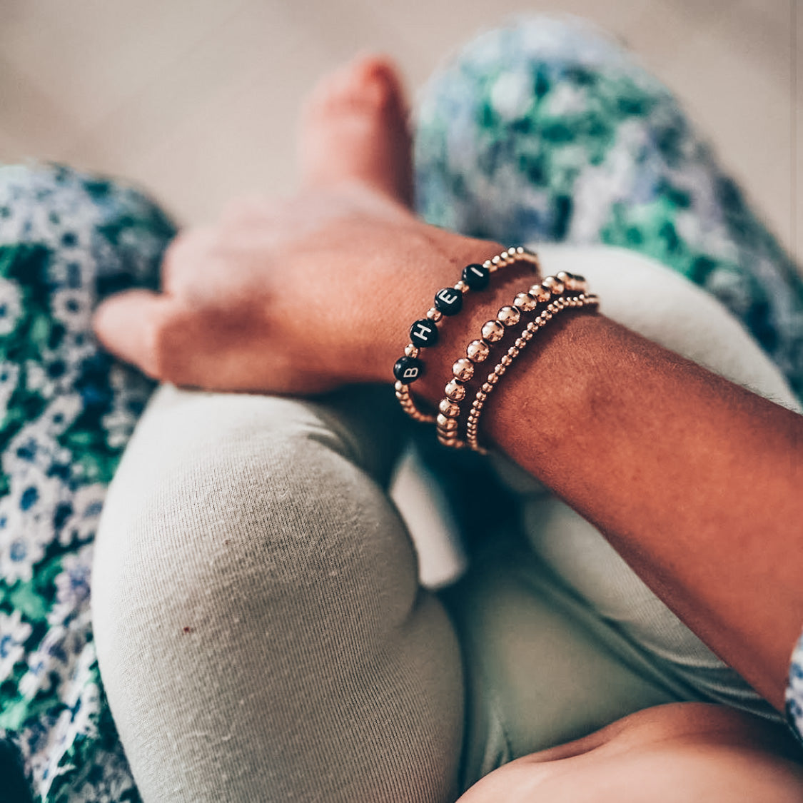 Model photo wearing stack of beaded bracelets with 4mm gold custom name bracelet in black letters