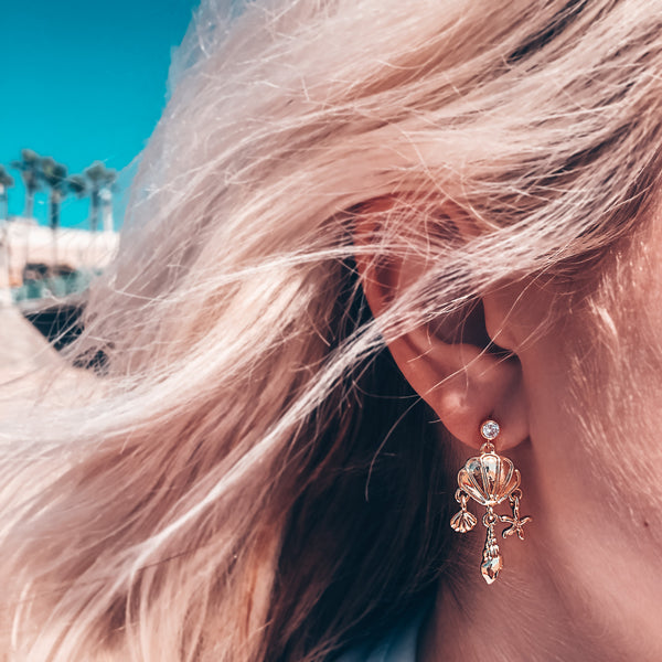 Model photo wearing CZ stud post with dangling seashell charms 14k gold-filled earrings
