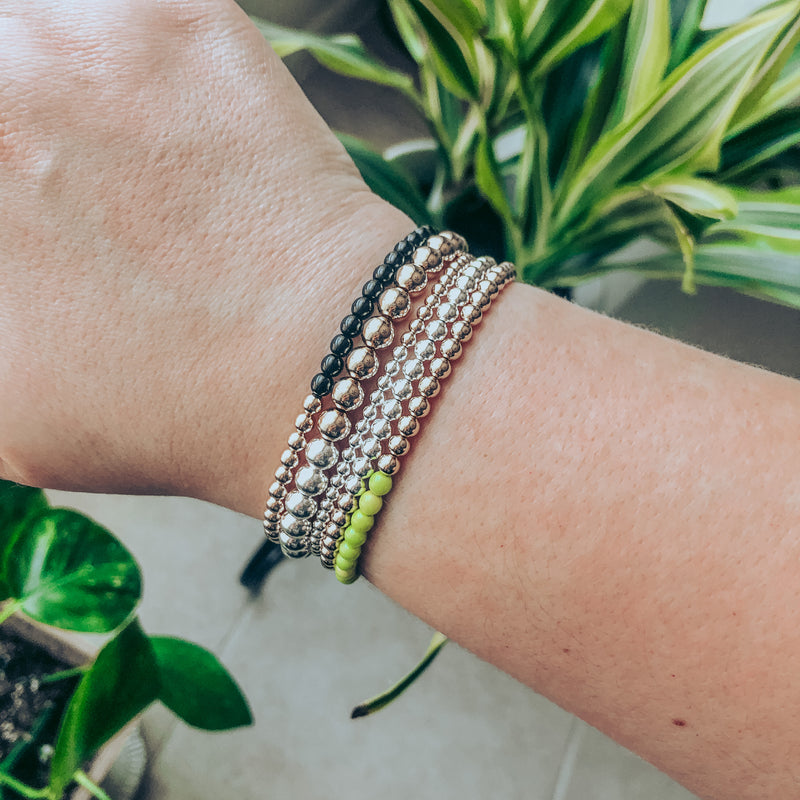 Model photo wearing triple stack of half 14k gold-filled and half sterling silver beaded bracelets in 3mm, 4mm, and 6mm bead sizes