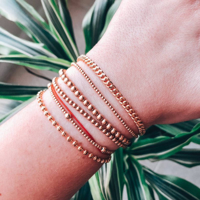 Model photo wearing a stack of classic gold bracelets including 14k gold-filled dainty minimal curb chain bracelet with extender