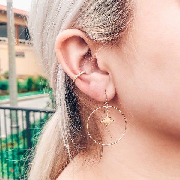 Model photo wearing 14k gold-filled dangle hoops with north star charm and gold ear cuff