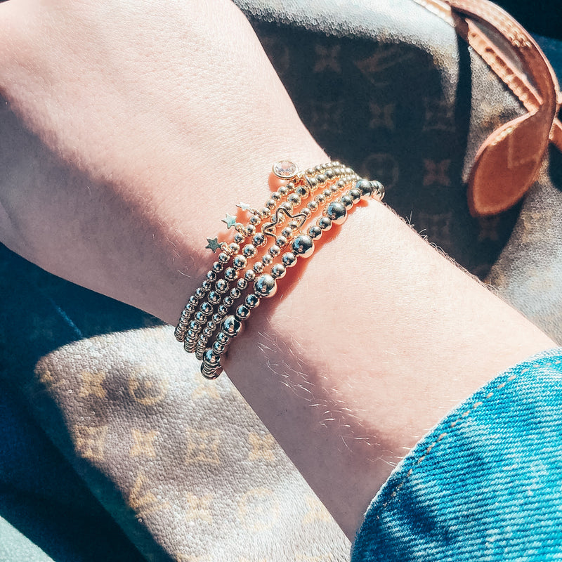 Model photo wearing stack of gold bracelets including 14k gold-filled beaded bracelet alternating 4mm and 6mm bead sizes