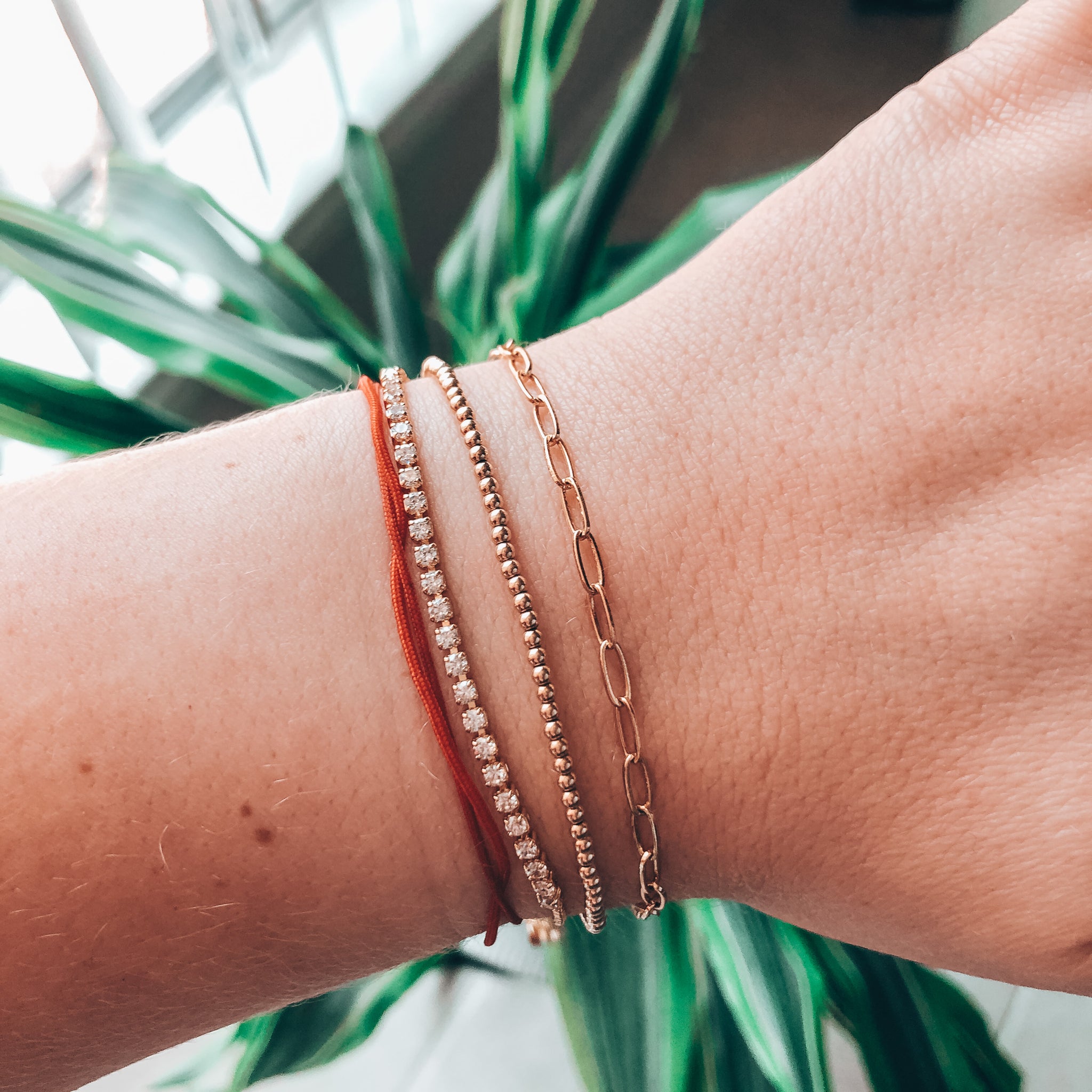 Model photo wearing stack of dainty bracelets including 14k gold-filled CZ tennis bracelet with box chain and bolo slider closure