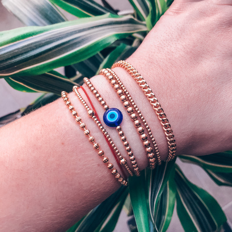 model photo wearing stacked bracelets including blue evil eye bead on 3mm 14k gold-filled beaded bracelet