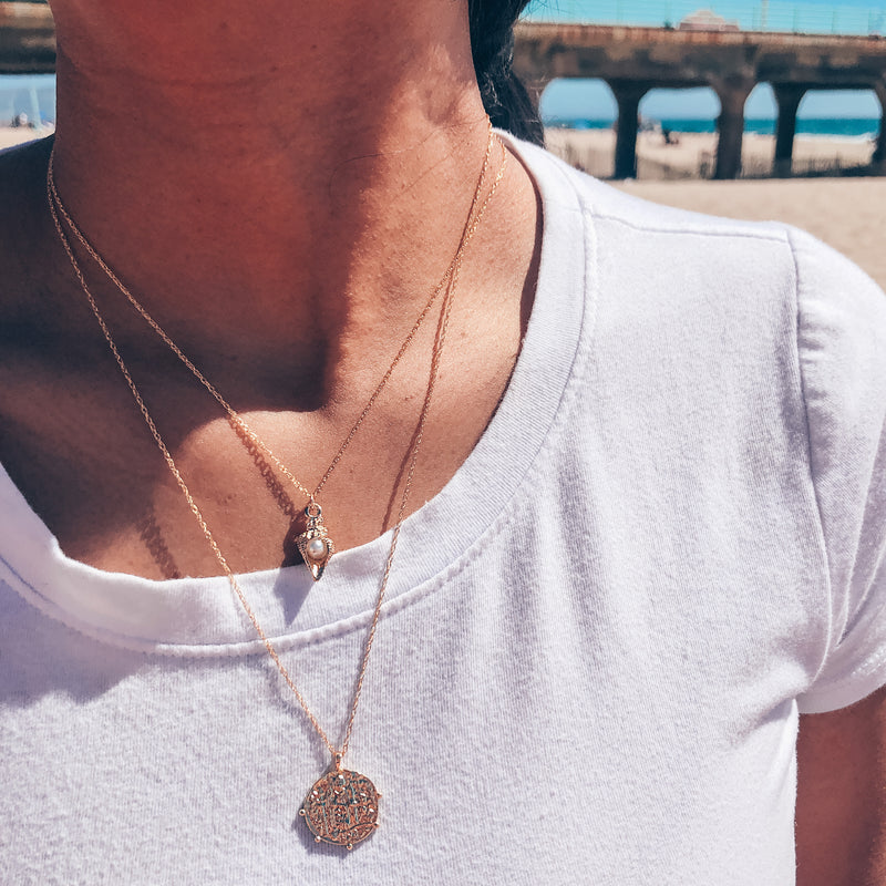 Model photo wearing layered gold necklaces including 14k gold-filled classic pirate coin necklace with scalloped edges