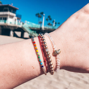 Model wearing stack of colorful golden beaded bracelets